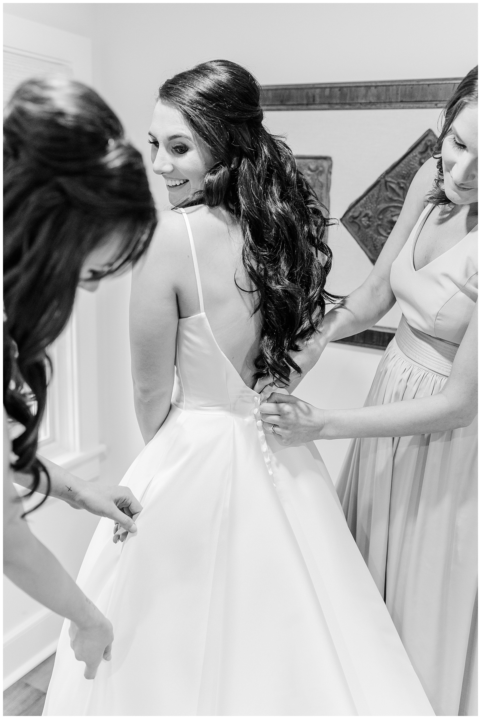 bridesmaids help bride button the back of her wedding dress with long train